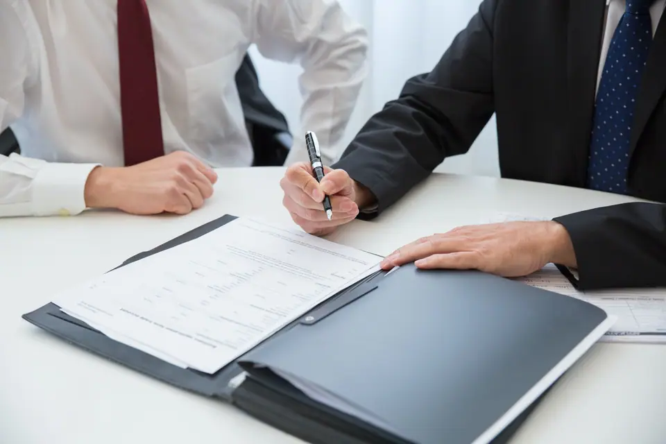 Dos personas firmando un contrato sobre una carpeta de documentos