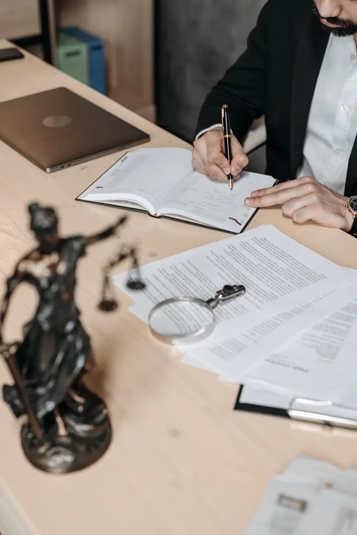 Documentos legales y una lupa sobre un escritorio, junto a la estatuilla de la Justicia